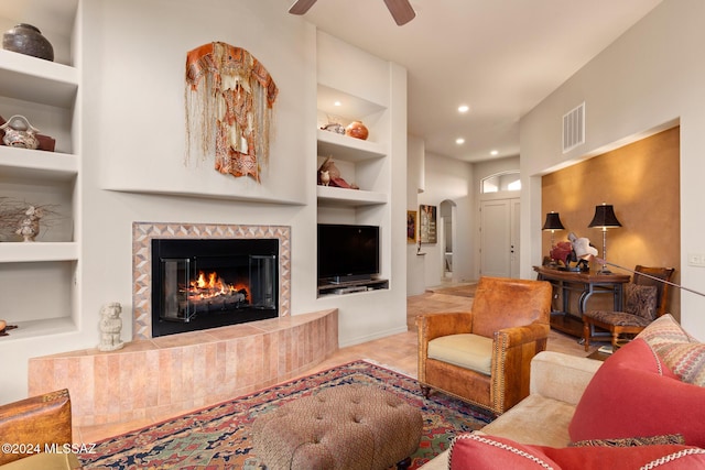 living room featuring built in shelves, ceiling fan, and a fireplace