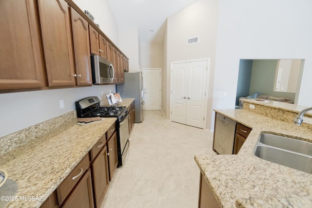 kitchen featuring light stone counters, sink, a towering ceiling, and appliances with stainless steel finishes