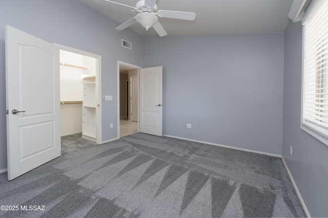 unfurnished bedroom with a spacious closet, ceiling fan, multiple windows, a closet, and dark carpet