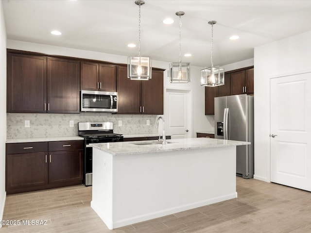kitchen featuring a sink, stainless steel appliances, light wood-type flooring, dark brown cabinetry, and hanging light fixtures