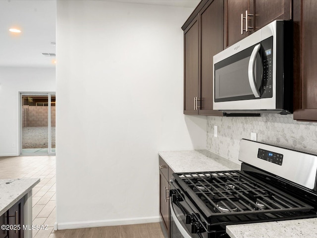 kitchen with dark brown cabinetry, light stone counters, decorative backsplash, stainless steel appliances, and visible vents