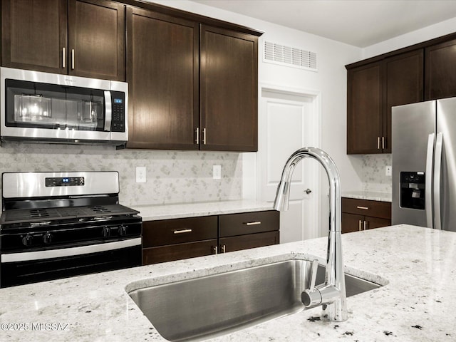 kitchen with a sink, dark brown cabinets, light stone counters, and stainless steel appliances