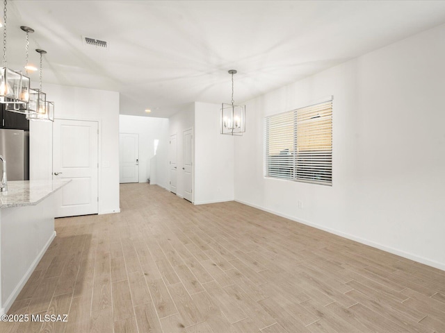 unfurnished dining area featuring light wood finished floors, visible vents, a chandelier, and baseboards