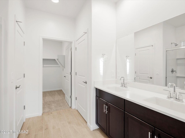 bathroom featuring wood finished floors, a shower stall, double vanity, and a sink
