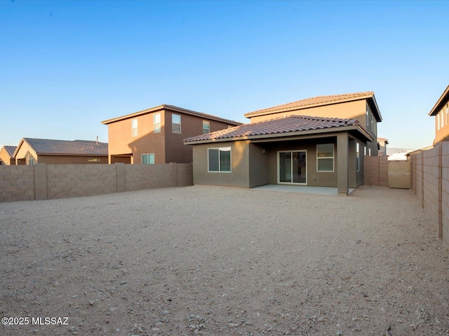 rear view of house featuring stucco siding, a tiled roof, a patio area, and a fenced backyard