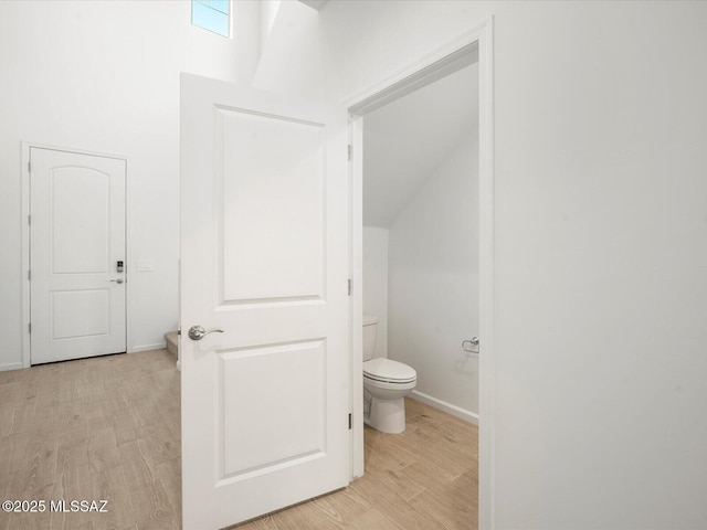 bathroom with lofted ceiling, wood finished floors, toilet, and baseboards