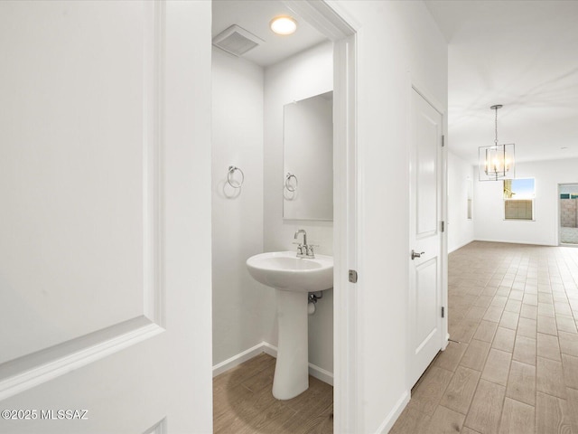 bathroom featuring a sink, visible vents, baseboards, an inviting chandelier, and wood finished floors