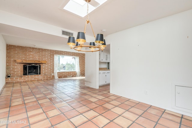 unfurnished living room with brick wall, a skylight, a chandelier, light tile patterned floors, and a brick fireplace