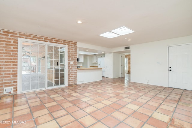 unfurnished living room featuring brick wall, light tile patterned floors, and a skylight