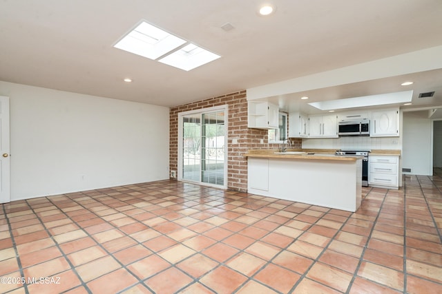 kitchen featuring light tile patterned floors, stainless steel appliances, kitchen peninsula, and white cabinets