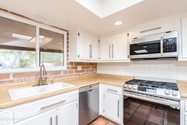 kitchen featuring sink, light tile patterned floors, appliances with stainless steel finishes, white cabinetry, and backsplash