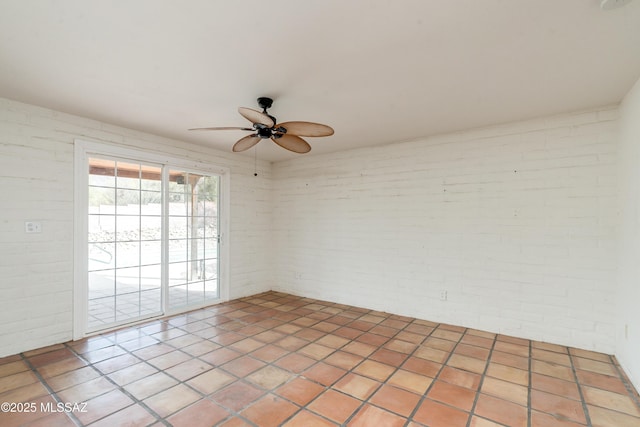 tiled empty room featuring ceiling fan and brick wall