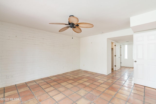 tiled spare room featuring ceiling fan and brick wall