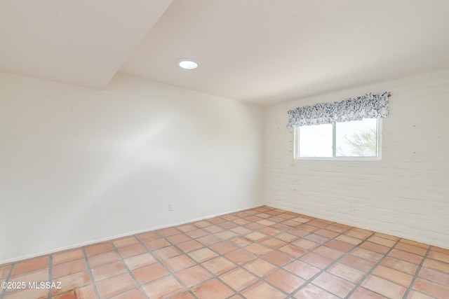 tiled empty room featuring brick wall