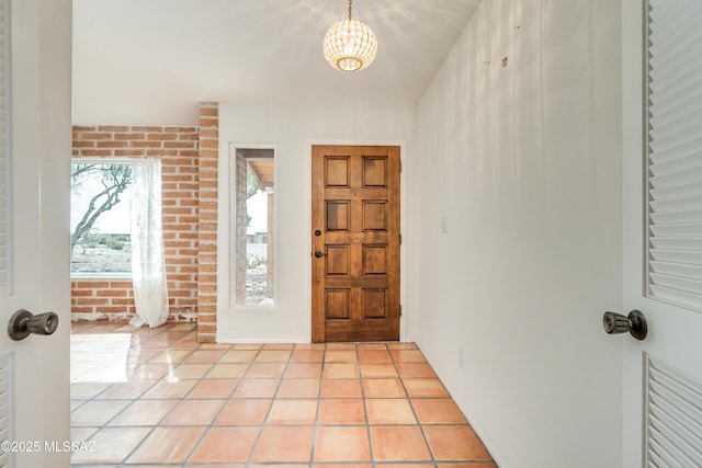 entrance foyer featuring a chandelier, brick wall, and light tile patterned flooring