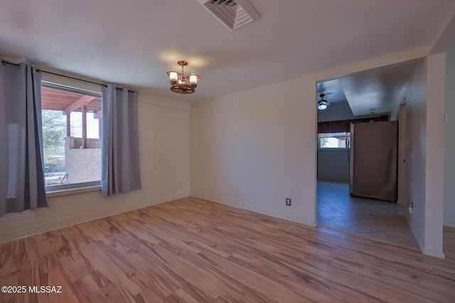 unfurnished room with ceiling fan with notable chandelier and light hardwood / wood-style flooring