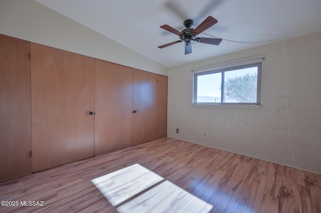 unfurnished bedroom featuring ceiling fan, light hardwood / wood-style floors, brick wall, and vaulted ceiling