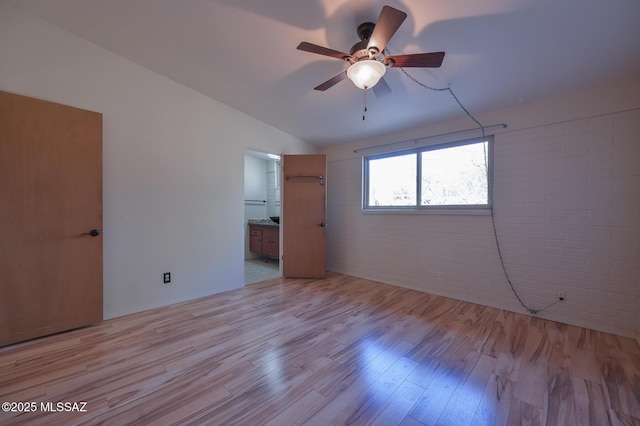 unfurnished bedroom featuring ceiling fan, brick wall, ensuite bathroom, lofted ceiling, and light wood-type flooring