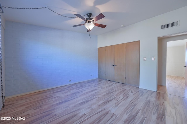 unfurnished bedroom with ceiling fan, a closet, brick wall, and light wood-type flooring