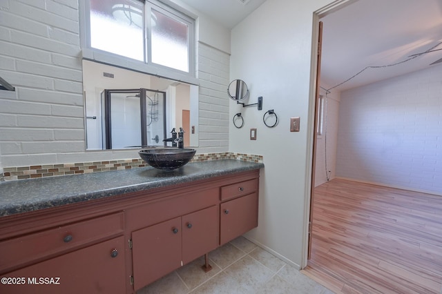 bathroom with tile patterned floors, vanity, a shower with shower door, and brick wall