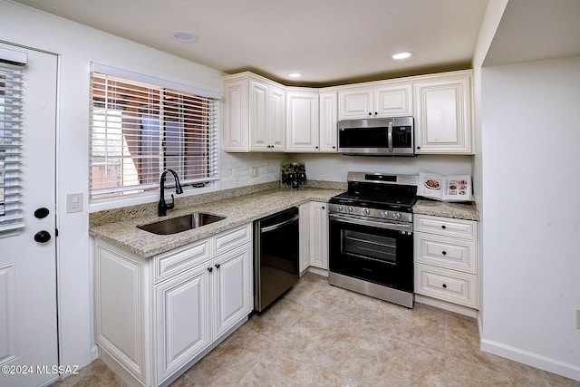 kitchen with light stone countertops, appliances with stainless steel finishes, white cabinets, and sink