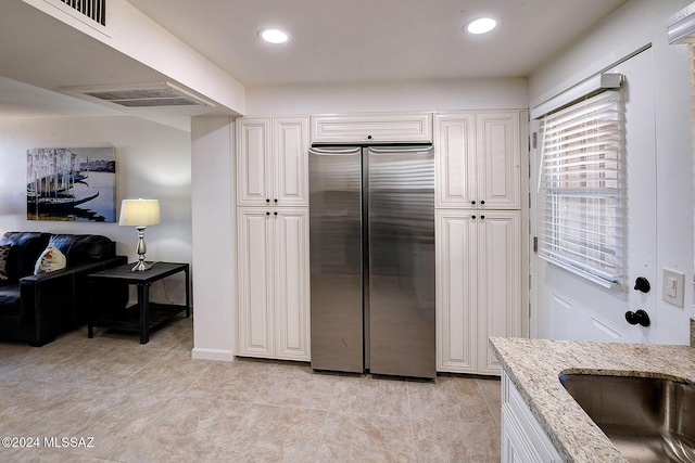 kitchen with sink, light tile patterned floors, light stone counters, white cabinetry, and stainless steel refrigerator