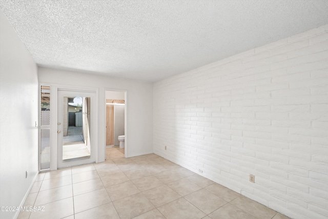 tiled spare room with brick wall and a textured ceiling