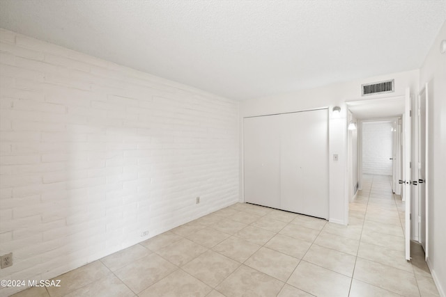 unfurnished bedroom with a closet, light tile patterned flooring, brick wall, and a textured ceiling