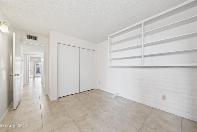 unfurnished bedroom featuring light tile patterned floors, brick wall, and a textured ceiling