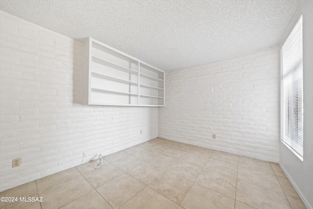 tiled spare room with brick wall, a healthy amount of sunlight, and a textured ceiling