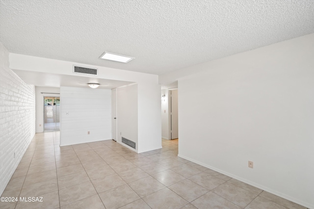 tiled empty room featuring a textured ceiling and brick wall