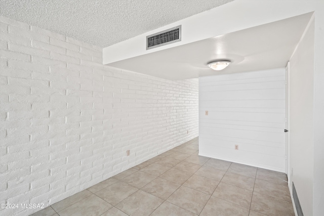 tiled spare room featuring brick wall and a textured ceiling