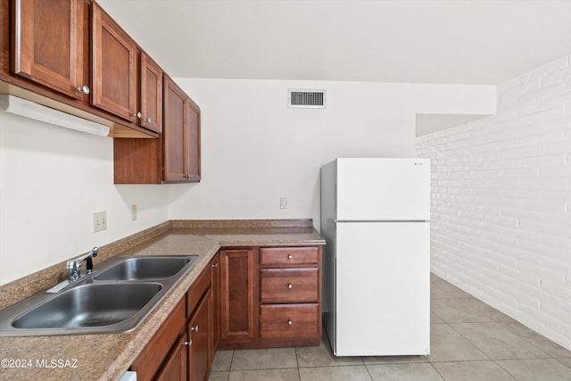 kitchen featuring white fridge, light tile patterned floors, sink, and brick wall