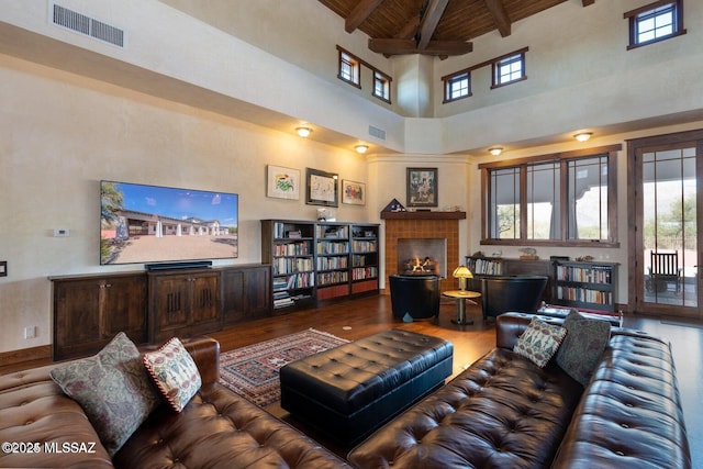 living room with wood ceiling, wood-type flooring, beam ceiling, a high ceiling, and a tiled fireplace