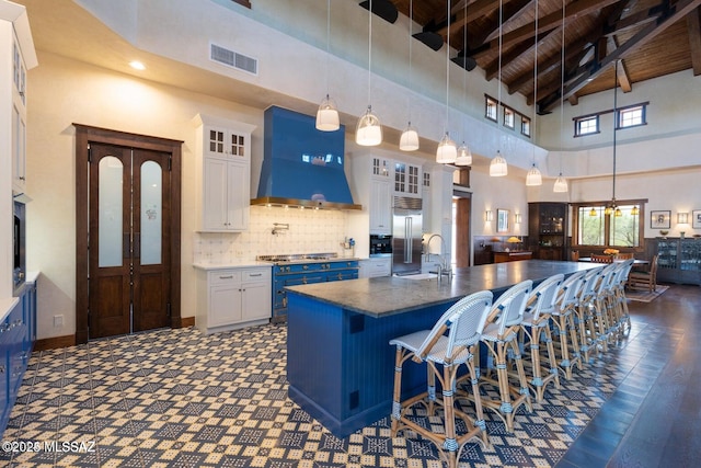 kitchen with premium range hood, a kitchen island with sink, beam ceiling, high vaulted ceiling, and white cabinetry