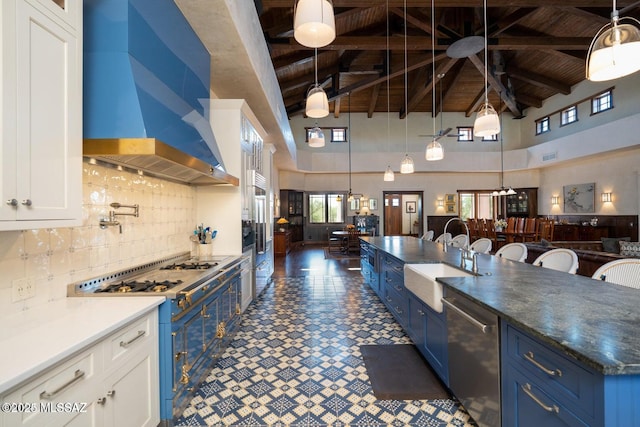 kitchen featuring range with two ovens, high vaulted ceiling, white cabinetry, and wall chimney exhaust hood