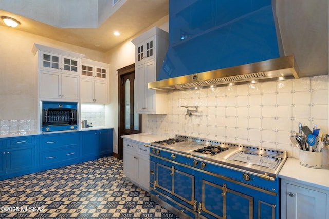 kitchen with white cabinets, wall chimney exhaust hood, blue cabinetry, and a high ceiling