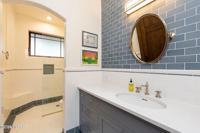 bathroom featuring tiled shower, vanity, toilet, and tile walls