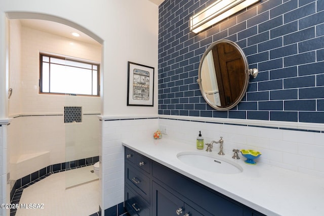 bathroom with a tile shower, vanity, and tile walls