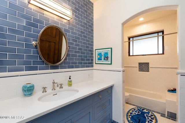 full bathroom with vanity, tile patterned floors, tiled shower / bath combo, toilet, and tile walls