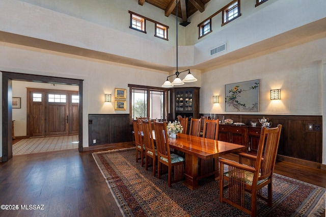 dining space with beamed ceiling, dark hardwood / wood-style floors, a towering ceiling, and a wealth of natural light