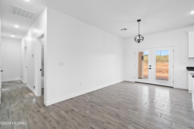 unfurnished dining area featuring a chandelier, french doors, and light wood-type flooring