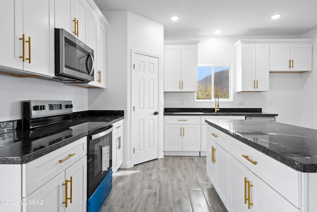 kitchen featuring dark stone counters, sink, light wood-type flooring, white cabinetry, and stainless steel appliances