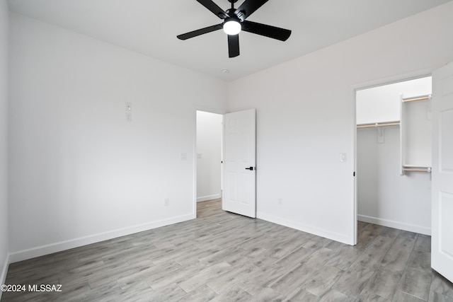 unfurnished bedroom featuring a closet, ceiling fan, light hardwood / wood-style flooring, and a walk in closet