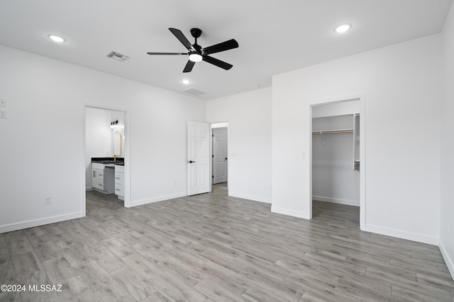 unfurnished bedroom featuring light hardwood / wood-style flooring, ceiling fan, a spacious closet, connected bathroom, and a closet