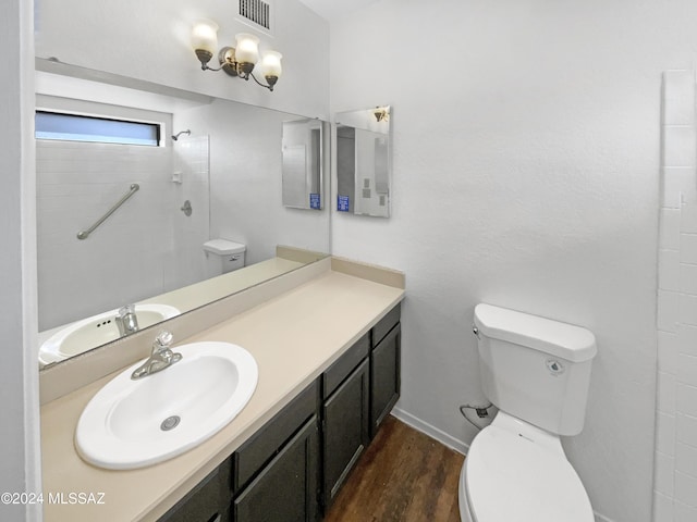 bathroom with hardwood / wood-style flooring, vanity, toilet, and tiled shower