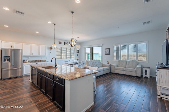 kitchen featuring appliances with stainless steel finishes, light stone counters, sink, white cabinets, and an island with sink