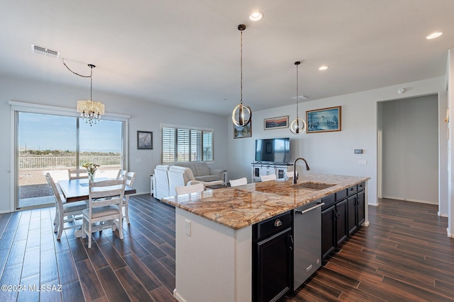 kitchen featuring light stone countertops, dishwasher, sink, an island with sink, and pendant lighting