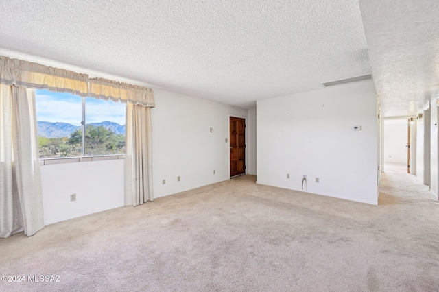 spare room featuring a mountain view, light carpet, and a textured ceiling