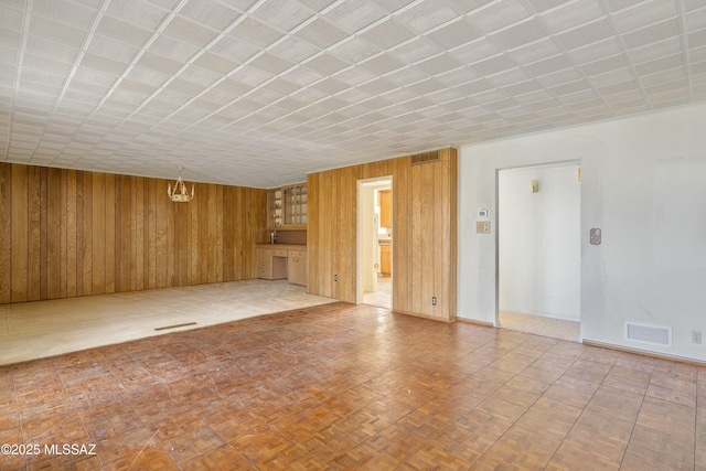 unfurnished living room featuring visible vents, baseboards, wooden walls, and an inviting chandelier